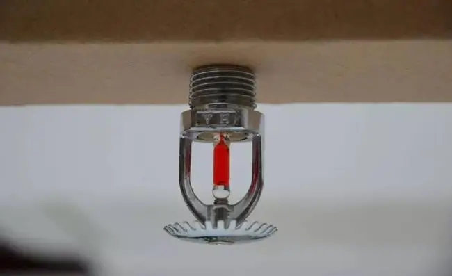 Close-up of a chrome automatic fire sprinkler head with a red heat-sensitive liquid bulb mounted on a ceiling.