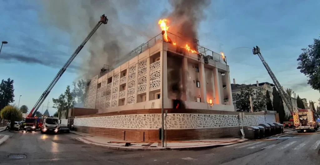 Firefighters using ladder trucks to extinguish a fire at a modern hotel building