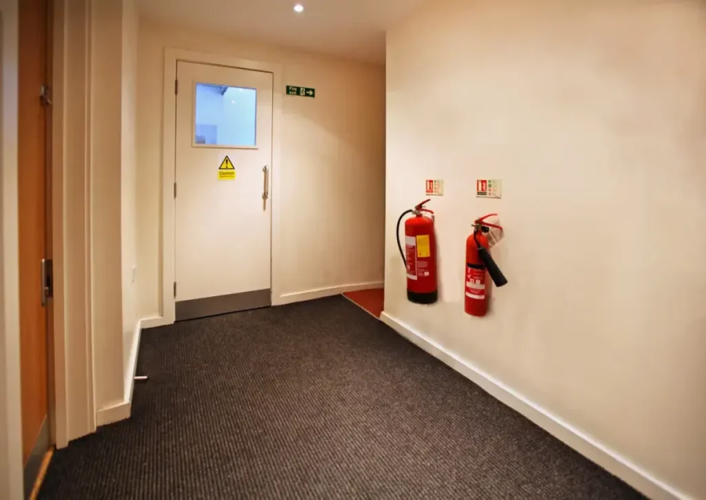 Clean hotel corridor with fire extinguishers and emergency exit signs