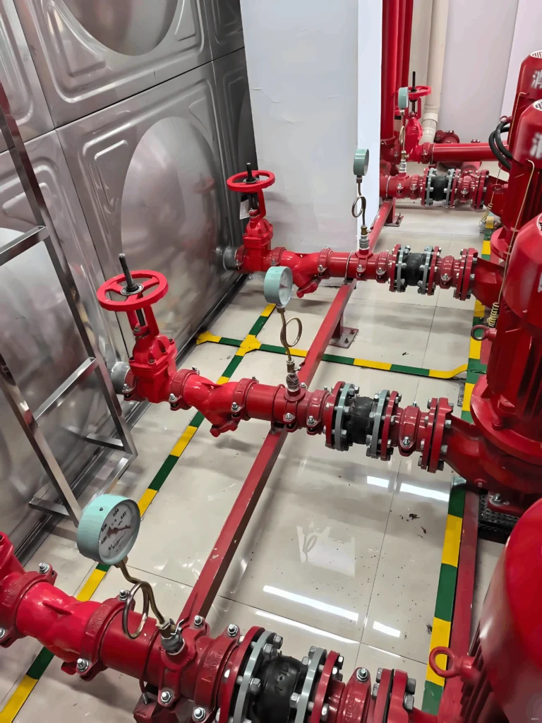 Red fire protection water pipelines with control valves and pressure gauges installed in a commercial building pump room.