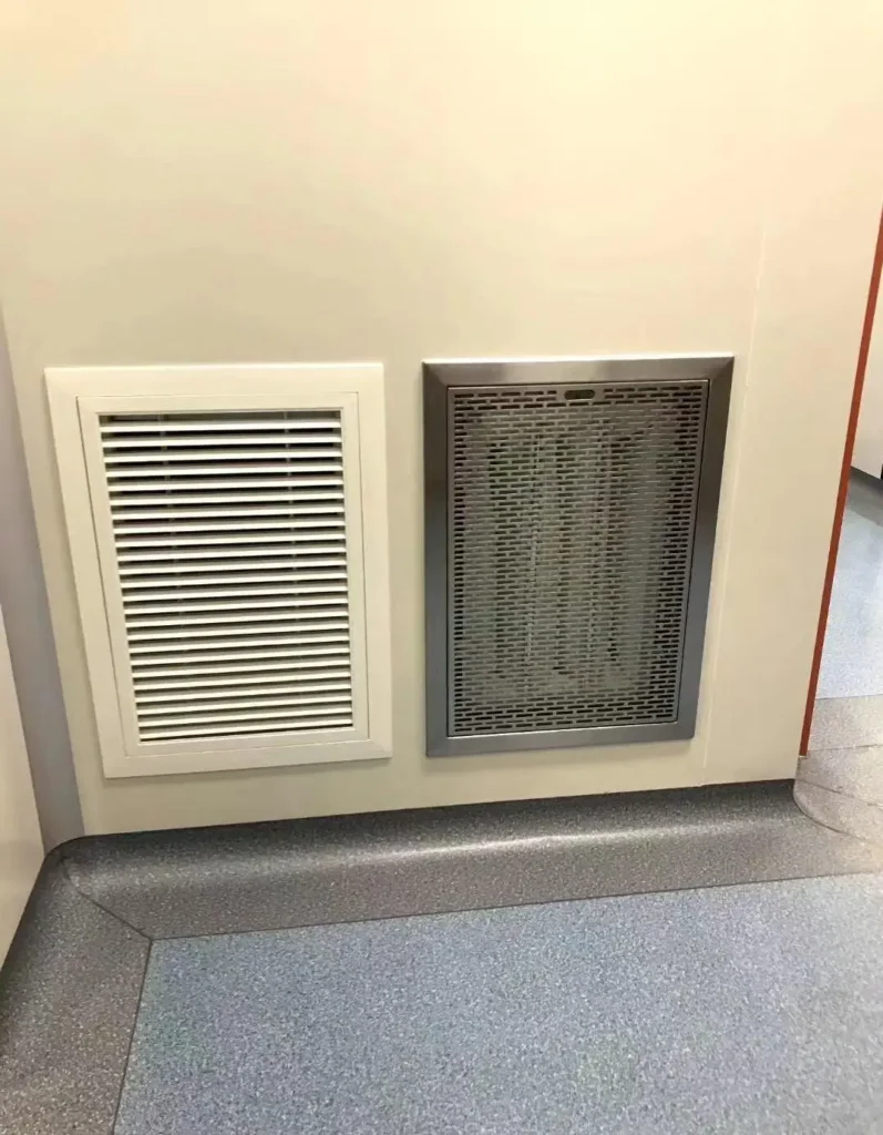 A low-wall air return grille and stainless steel mesh exhaust vent installed in a dust-free GMP cleanroom with curved PVC flooring.