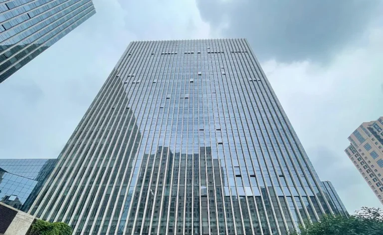 Low-angle view of Guancheng Mansion, a modern high-rise commercial office building with a glass curtain wall facade under a cloudy sky.