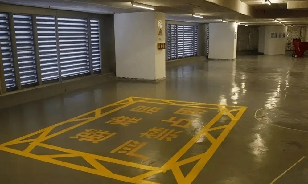 An empty underground parking lot featuring a glossy gray anti-slip epoxy floor with a yellow fire lane no parking warning sign.